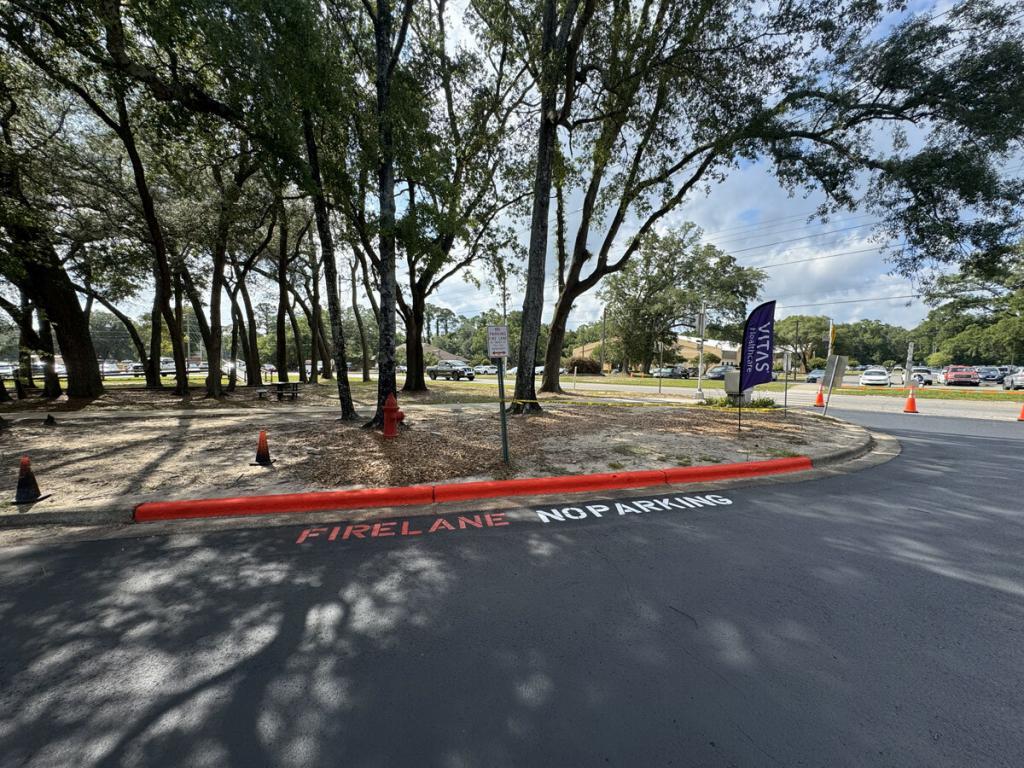 Crew striping fresh parking lines and applying sealcoat on asphalt lot with safety cones
